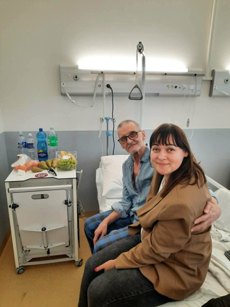 Socialinės pagalbos darbuotoja lydi senjorą vežimėlyje gamtoje
